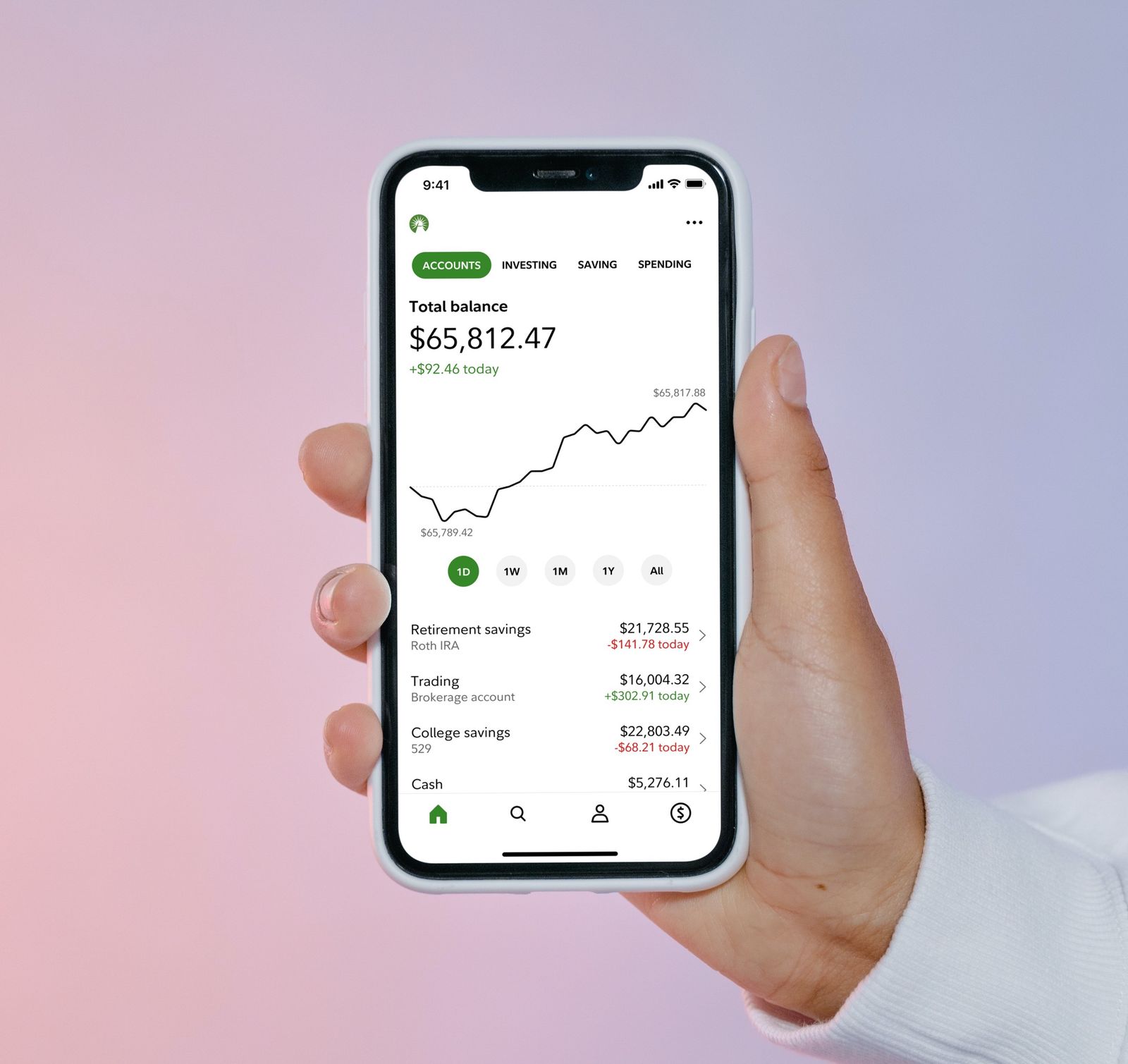 A hand holding an iPhone showing the redesigned Fidelity app home screen, with a total balance, a performance chart and a list of accounts.